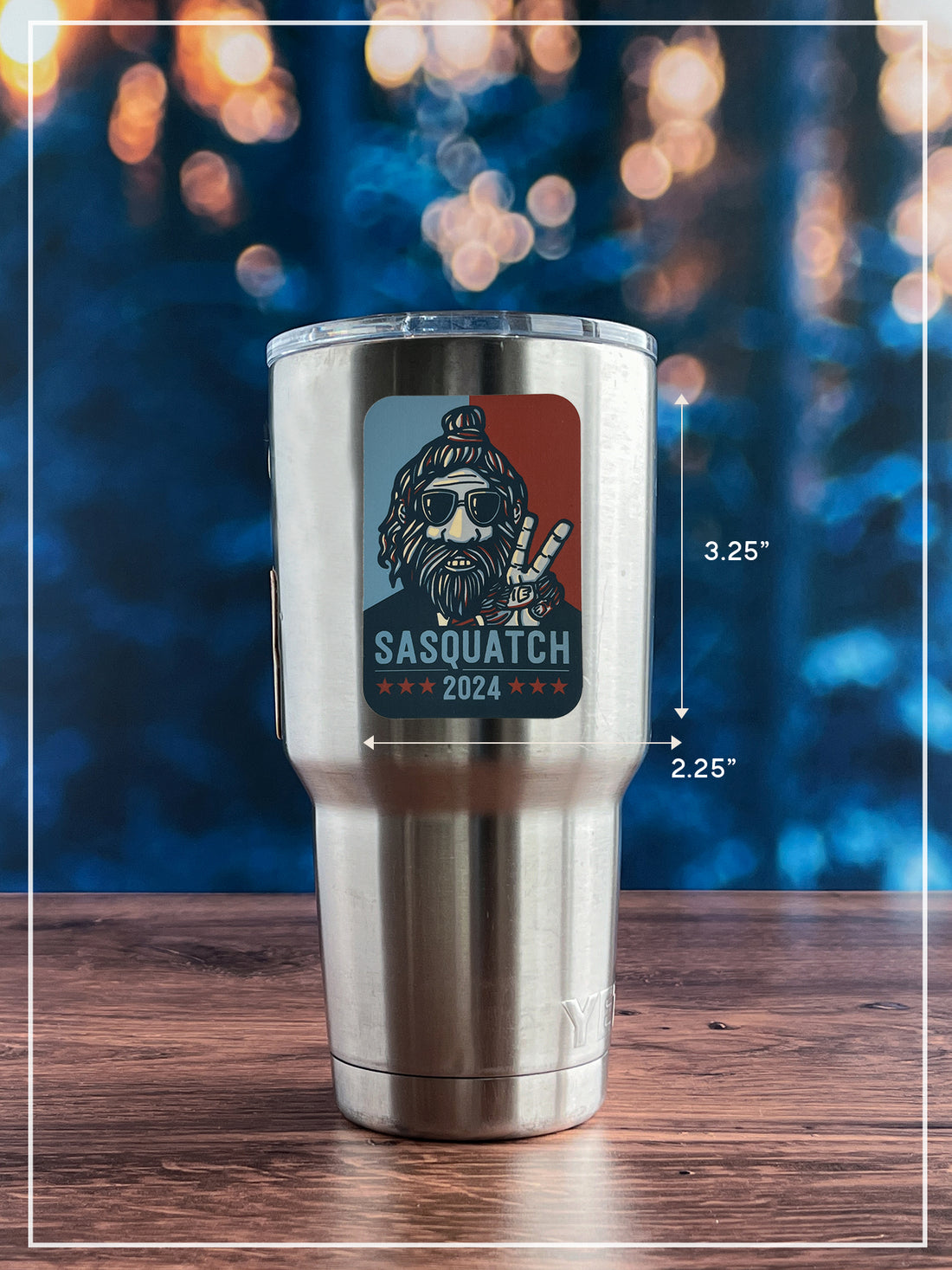 Sasquatch 2024 sticker placed on stainless steel insulated cup. Trees and lights in the far background.